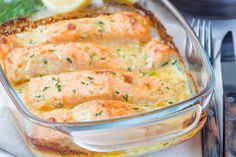 a glass casserole dish with salmon and cheese on the side next to a fork