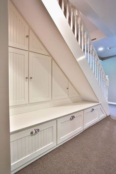 an empty room with white cabinets and drawers under the stair case in this attic space