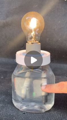 a person pointing at a light bulb on top of a glass container with an object inside it