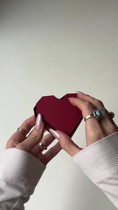 a woman holding a red heart shaped box in her right hand with two rings on it