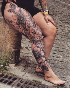 a woman sitting on top of a wooden bench next to a brick wall with tattoos on her legs