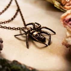 a spider necklace with a skull on it's face sitting next to some flowers