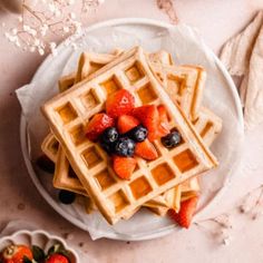 waffles with strawberries and blueberries on a white plate next to flowers