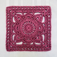 a pink crocheted square on top of a white table cloth