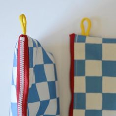 two blue and white checkered bags with yellow handles hanging from hooks on the wall