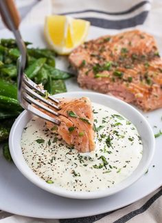 a white plate topped with salmon and greens next to a fork on top of it