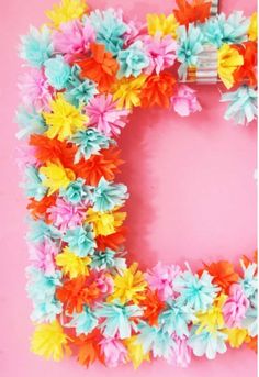 a colorful paper flower wreath on a pink background with the letter d in the middle