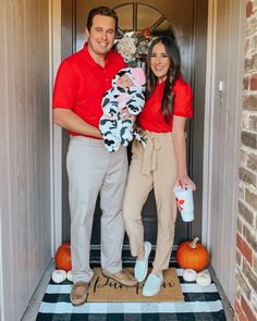 a man and woman standing in front of a door holding a baby wearing a costume