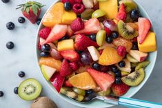 a bowl filled with fresh fruit on top of a table next to sliced kiwis and strawberries