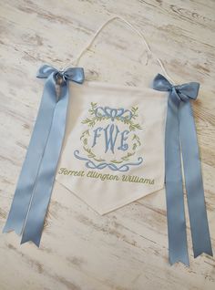 an embroidered banner hanging on a wooden table with blue ribbon around it that says fw