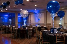 blue and white balloons are hanging from the ceiling in an elegant banquet hall decorated with black table cloths