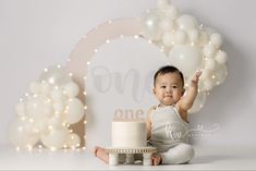 a baby sitting in front of a cake with balloons