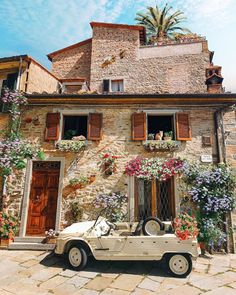 an old car parked in front of a building with flowers growing on the windows and doors