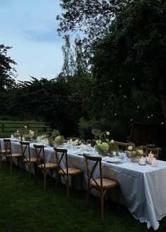 a long table is set up with white linens and candles for an outdoor dinner