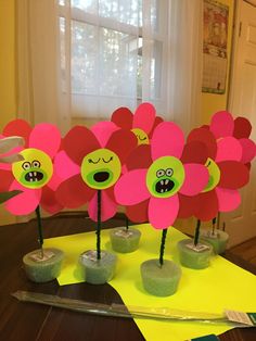 three paper flowers with faces on them sitting on top of a table in front of a window