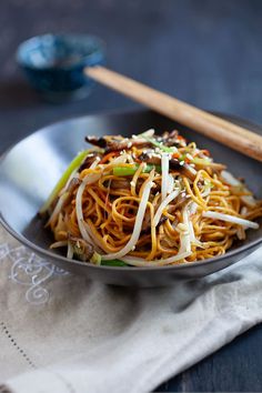 a black plate topped with noodles and vegetables next to chopsticks on a table