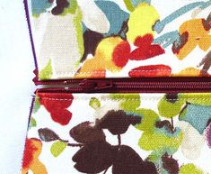 a colorful floral print purse with zippers on the front and side, sitting on a white surface