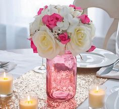 a vase filled with white and pink flowers on top of a table next to candles