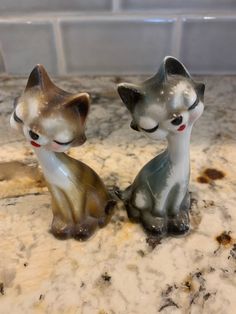 two small figurines sitting on top of a marble counter