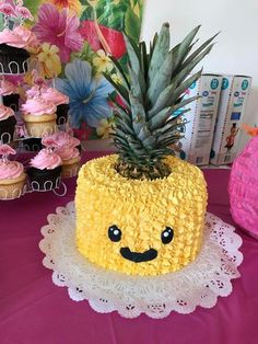 a pineapple shaped cake on a doily with cupcakes in the background