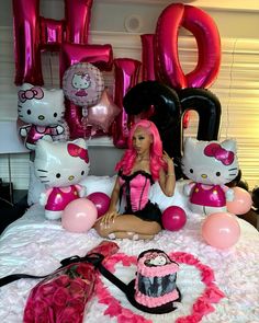 a barbie doll sitting on top of a bed next to pink and black hello kitty balloons