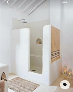 a white bathroom with an open shower stall and rugs on the floor next to it