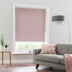 a living room with pink roller shades on the window and a grey couch in front