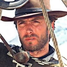 a man wearing a hat and holding two large metal scissors in his hand while looking at the camera