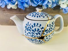 a blue and white tea pot sitting on top of a table next to some flowers