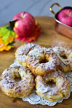 some sugared donuts on a doily with apples in the background