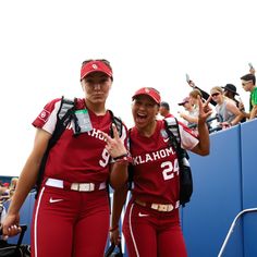 two women in red uniforms standing next to each other at a baseball game with fans behind them