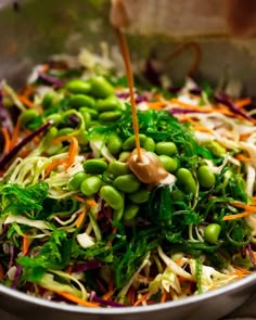 a bowl filled with vegetables and dressing being poured onto it's salad mixtures