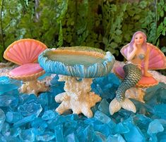 two little mermaid figurines sitting on top of blue rocks