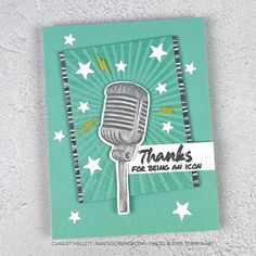 a handmade thank card with a microphone and stars in the background on a white surface