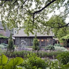 a garden with lots of plants and flowers in front of a building that has a fountain on it