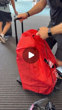 a man pulling a red piece of luggage across an airport floor with other people in the background