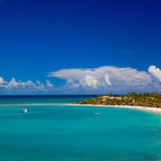 a boat is in the clear blue water near an island with palm trees and white sand