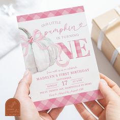 a person holding up a pink and white birthday card with a small pumpkin on it