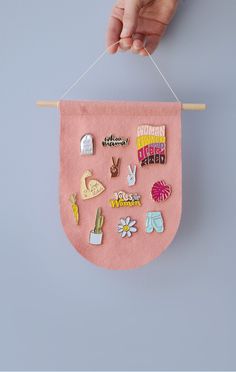 a hand holding a pink banner with various pins on it hanging from a clothes line