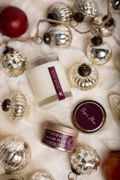 an assortment of christmas ornaments and candles on top of a white fur covered tablecloth