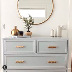 a white dresser with gold handles and a round mirror above it