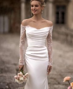 a woman in a white wedding dress holding a bouquet and posing for the camera with her hands on her hips