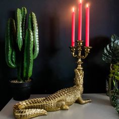 a gold alligator statue sitting on top of a table next to a candle holder and cactus