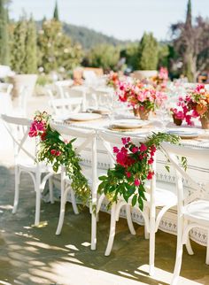 an outdoor dining table set with white chairs and pink flowers on each chair for seating