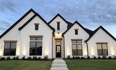 a large white house with black trim and lights on the front door is lit up at night