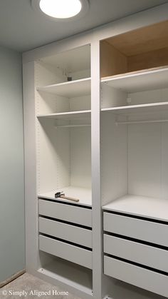 an empty walk - in closet with white shelves and drawers on the bottom shelf, next to a light fixture