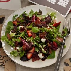 a white plate topped with a salad next to a fork and knife on top of a table