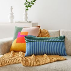 pillows on a couch in front of a vase with a plant and other decorative items