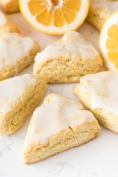 lemon scones with white icing on a marble counter top next to sliced lemons