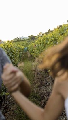 a woman holding her hair in front of a man who is walking through a vineyard